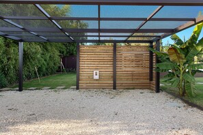 A covered outdoor area with a wooden fence, a metal mesh roof, and a gravel ground.