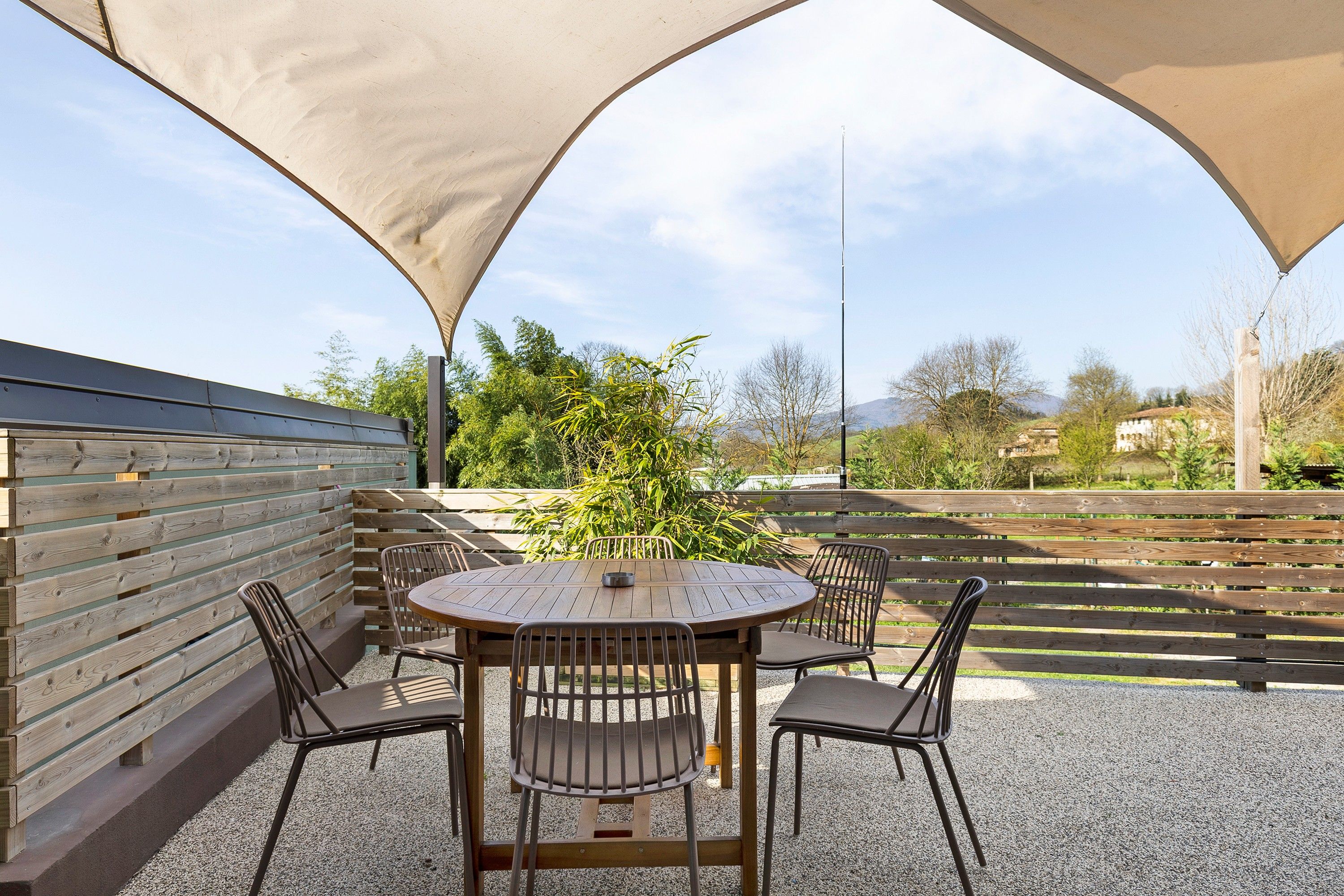 Eine Terrasse im Freien mit einem runden Tisch und Stühlen, umgeben von einem Holzzaun und einer großen Markise.