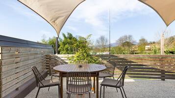 Eine Terrasse im Freien mit einem runden Tisch und Stühlen, umgeben von einem Holzzaun und einer großen Markise.