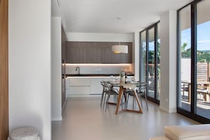 A modern kitchen with a dining area, large windows, and a view of the outdoors.