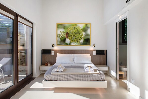 A modern bedroom with a large bed, a wall-mounted painting, and a glass door leading to an outdoor area.