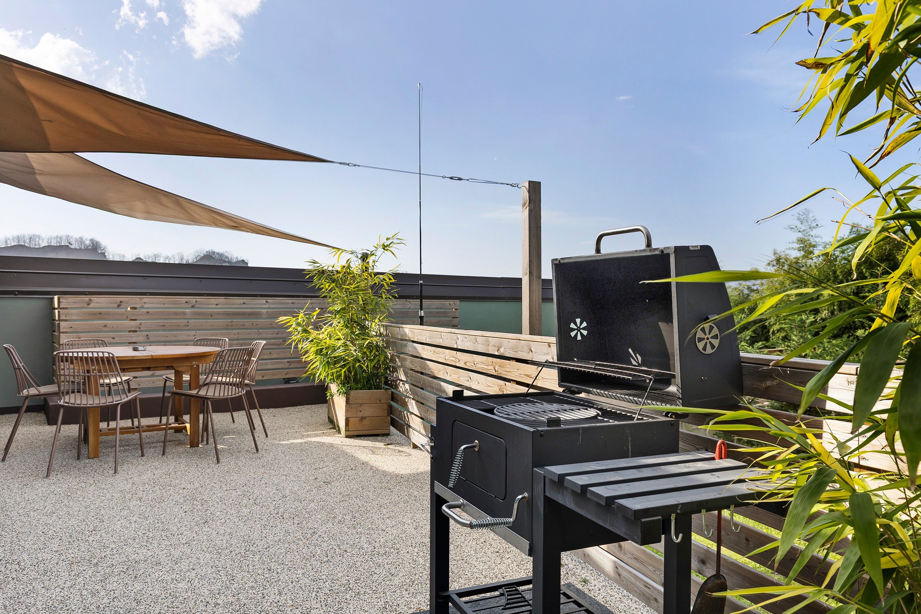 Eine Terrasse mit Grill, Tisch, Stühlen und einem Blumentopf.