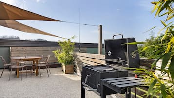 Eine Terrasse mit Grill, Tisch, Stühlen und einem Blumentopf.