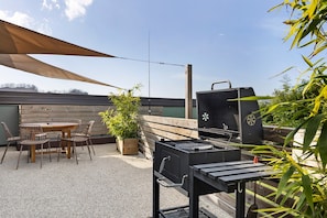 Eine Terrasse mit Grill, Tisch, Stühlen und einem Blumentopf.