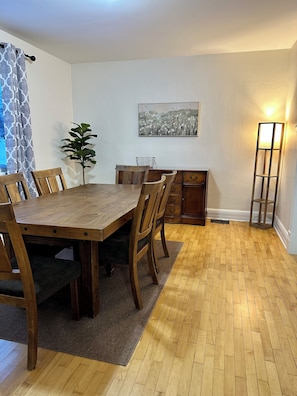 A dining area with a wooden table and chairs, a potted plant, a painting on the wall, and a floor lamp. - Charming Copper Country Mining House (Calumet)