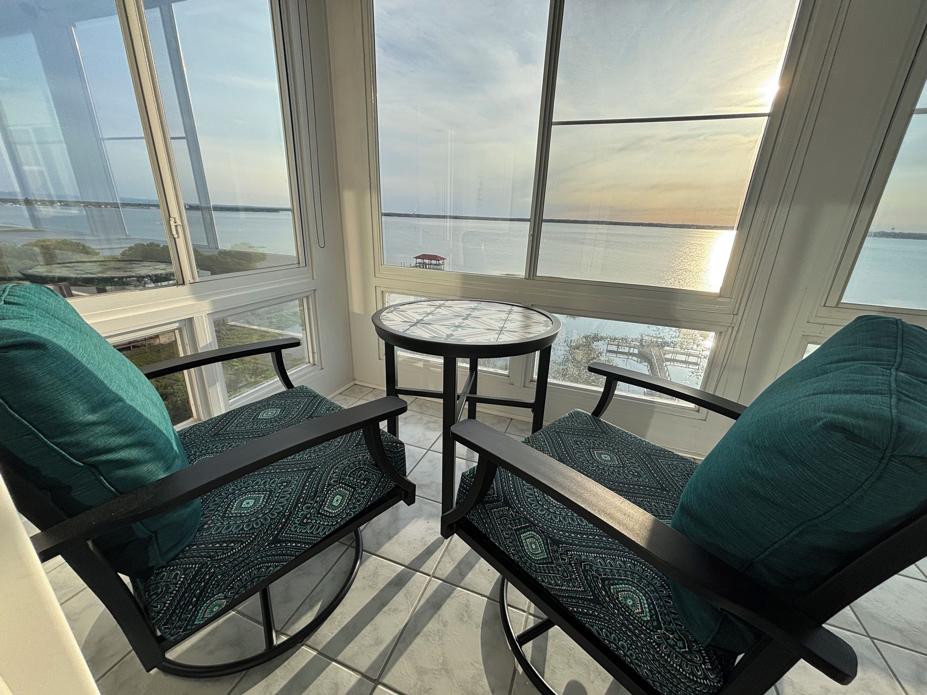 A balcony with two chairs and a small table, overlooking a body of water and a distant structure.