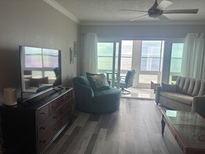Ein Wohnzimmer mit Fernseher, einer Couch, einem Sessel und einem Glastisch.