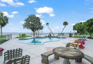 A pool area with a curved edge, lounge chairs, and a view of the water. - Lakefront Luxury - Sunset Views - Walk to Circle (Sebring)