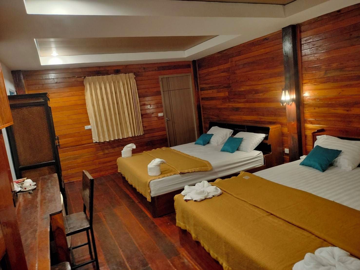 A hotel room with two beds, wooden walls, a desk, and a chair.