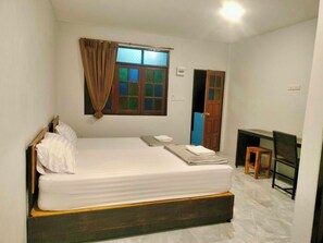 Habitación individual con una cama, cabecera de madera, ventana con cortinas, mesita de noche y un taburete pequeño de madera.