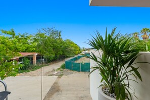 Ein Balkon mit Blick auf einen Feldweg, viel Grün und ein eingezäuntes Gelände.
