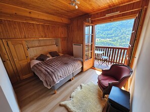 A wooden cabin bedroom with a bed, a chair, a small table, and a view of a forest through an open door. - Beautiful cabin for 12–14 people. Winter/Summer in Vaujany, the Greater Alpe d'Huez Area (Vaujany)