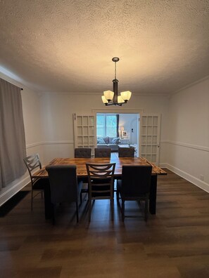 A dining room with a wooden table and chairs, a chandelier, and a view into another room with a sofa and a window. - Charming 3-bedroom house Cincinnati (Cincinnati)