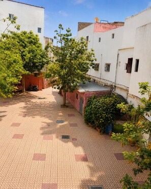 A courtyard with a tiled floor, surrounded by buildings with white walls and a tree providing shade. - petite maison traditionnelle à l ancienne médina à Casablanca (Casablanca)