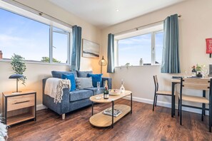 A modern living room with a sofa, coffee table, and a dining area with a chair and table. - Spacious Burslem Studio Perfect for Contractors (Stoke-on-Trent)