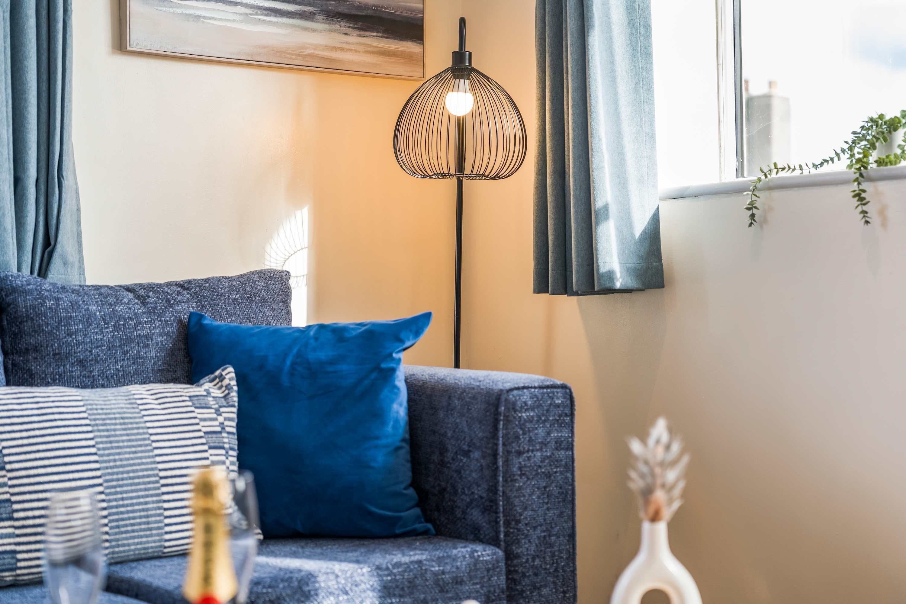 Una sala de estar con un sofá, una lámpara de pie y un ventanal con cortinas.