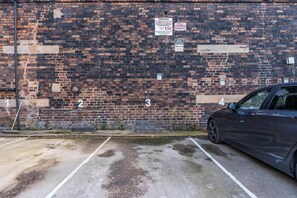 A parking area with a brick wall, multiple parking spaces, and a car parked in one of the spaces. - Stylish Burslem Studio Perfect for Contractors (Stoke-on-Trent)