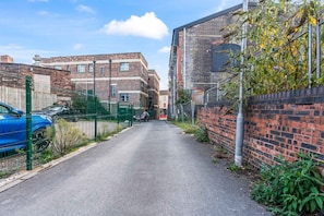 A narrow street flanked by residential buildings, a blue car parked on the left, and a metal fence. - Stylish Burslem Studio Perfect for Contractors (Stoke-on-Trent)