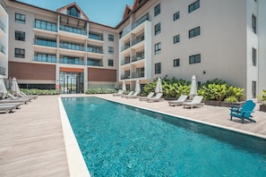 A modern hotel with a swimming pool, multiple balconies, and lounge chairs. - Elegant and Sophisticated Apartment Near the Beach (Punta Cana)