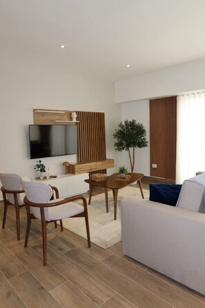 A modern living room with a flat-screen TV, wooden furniture, a white sofa, and a small table with a plant. - Elegant and Sophisticated Apartment Near the Beach (Punta Cana)