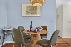 A dining area with a round wooden table, four green upholstered chairs, a wicker pendant light, and a framed map on the wall. - Wineberry Ridge Hot Tub Sauna Grill Views (Asheville)