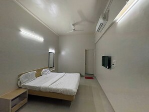 Un dormitorio pequeño y bien iluminado con una cama individual, una mesita de noche, un espejo, un ventilador de techo y un televisor montado.