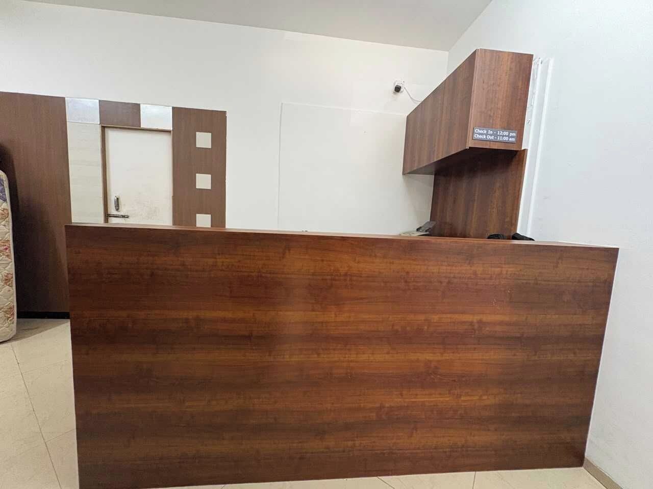 A reception desk with a wooden finish, a white wall, and a door in the background.