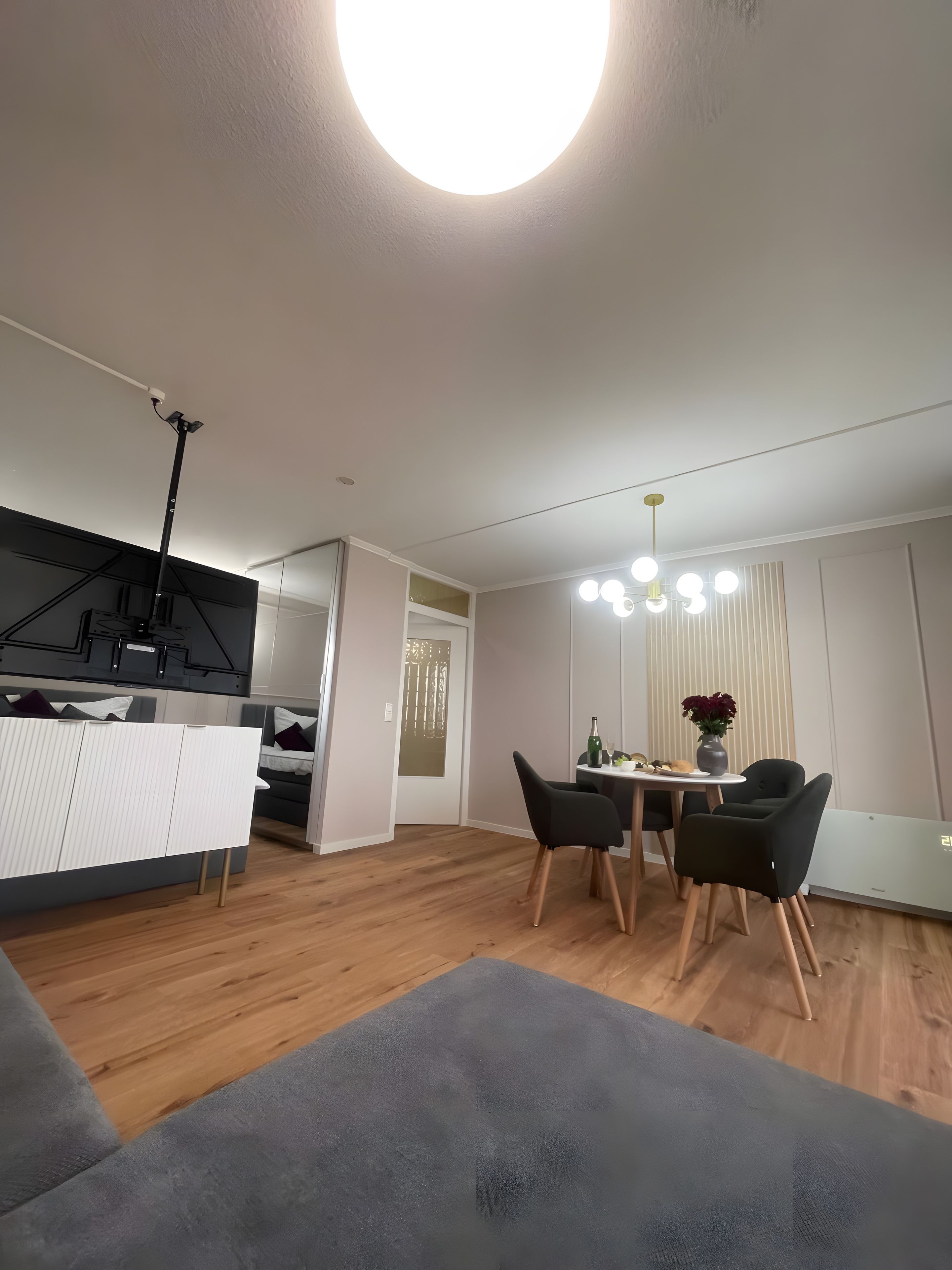 Ein modernes Wohnzimmer mit Essbereich, Holzboden und einer Deckenleuchte.
