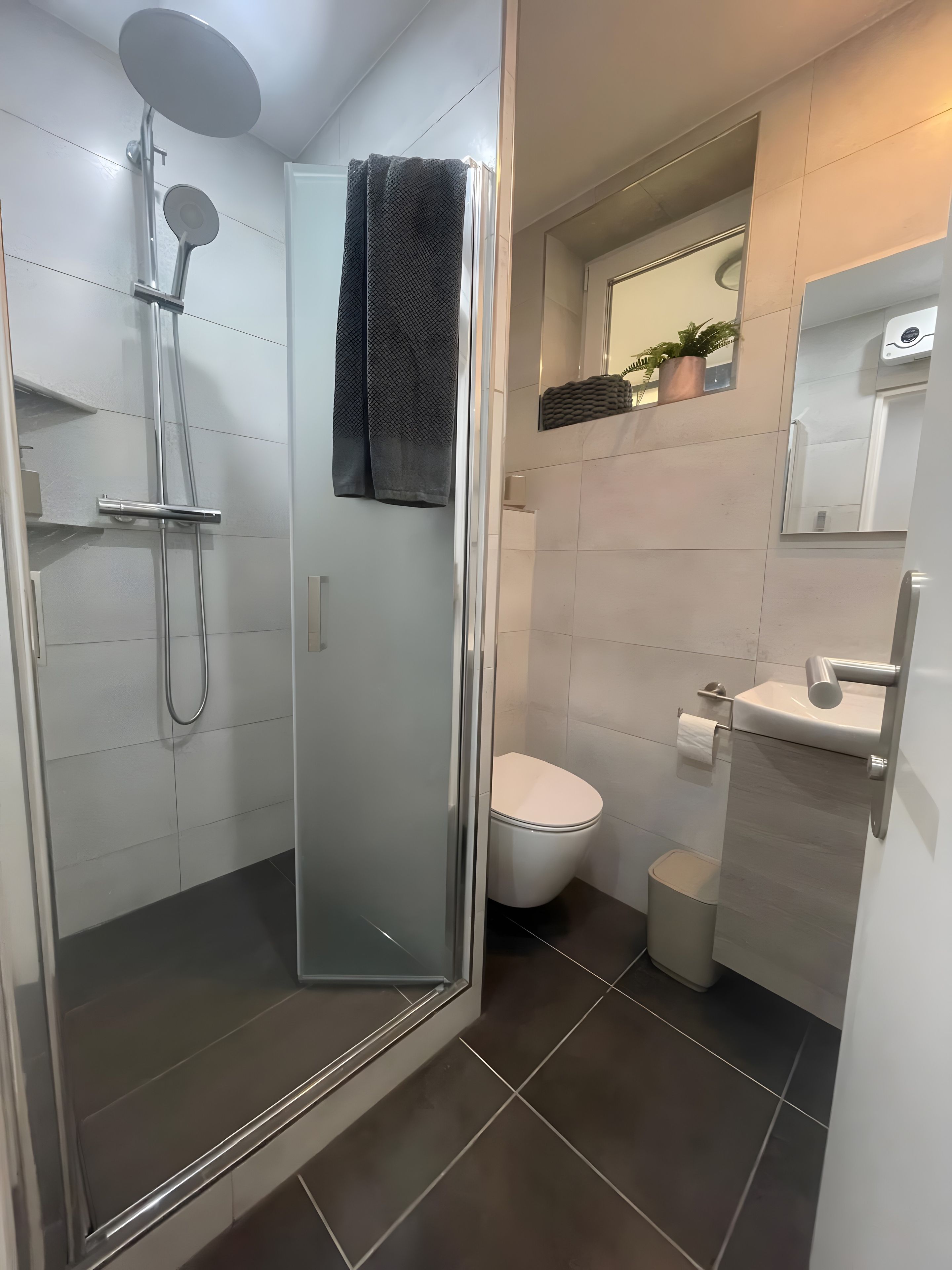 Ein modernes Badezimmer mit einer Glaskabine zur Dusche, einer Toilette und einem Waschbecken mit Spiegel darüber.