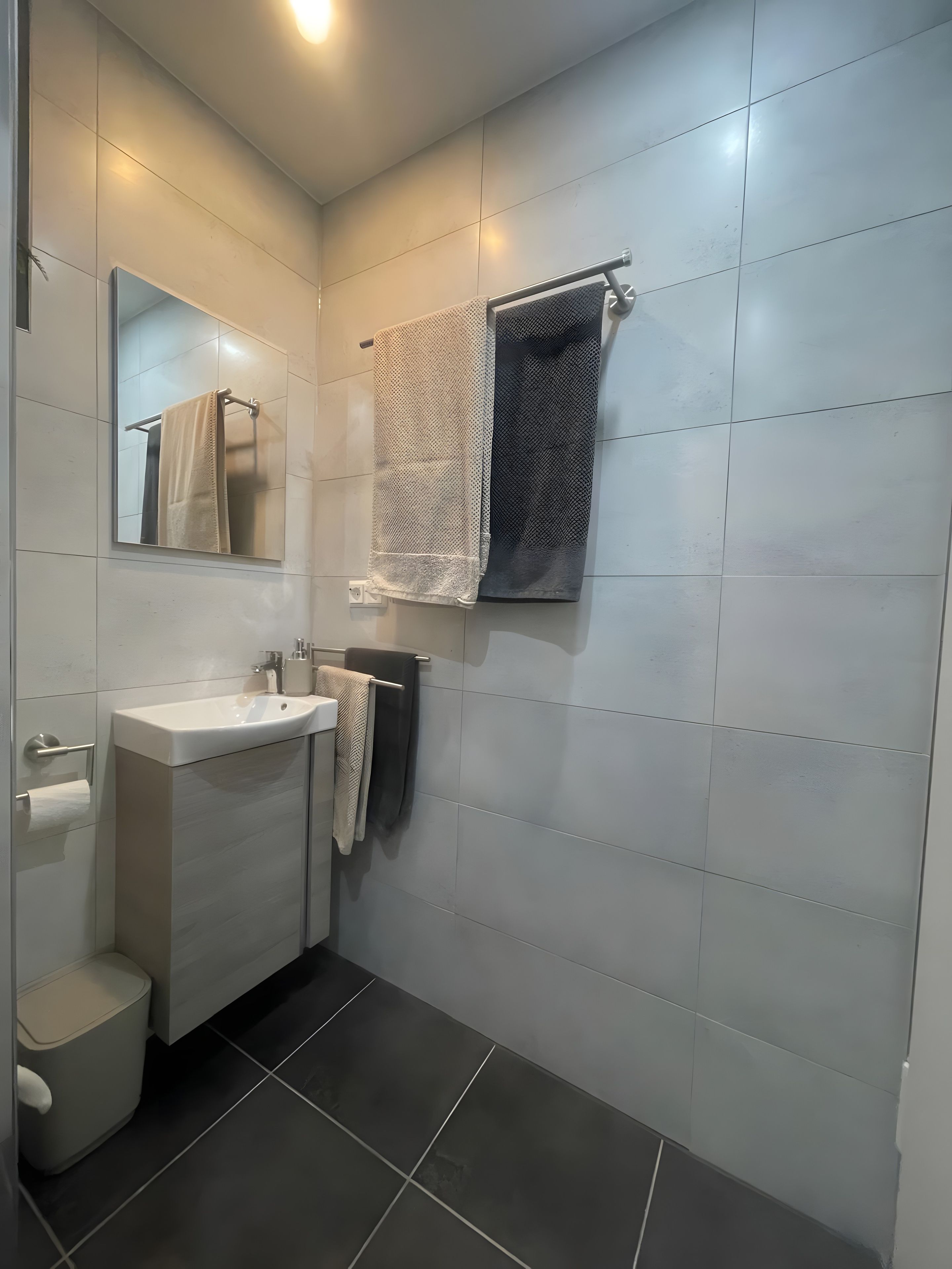 Ein modernes Badezimmer mit einem weißen Waschbecken, einem Spiegel und zwei Handtüchern auf einem Ablagekorb.