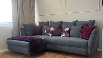 Ein modernes Wohnzimmer mit einem grauen Sofa, Holzboden und einem Fenster mit Vorhängen.