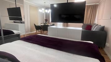 Una moderna camera d'albergo con un letto grande, una TV a schermo piatto, una scrivania con sedia e un divano.