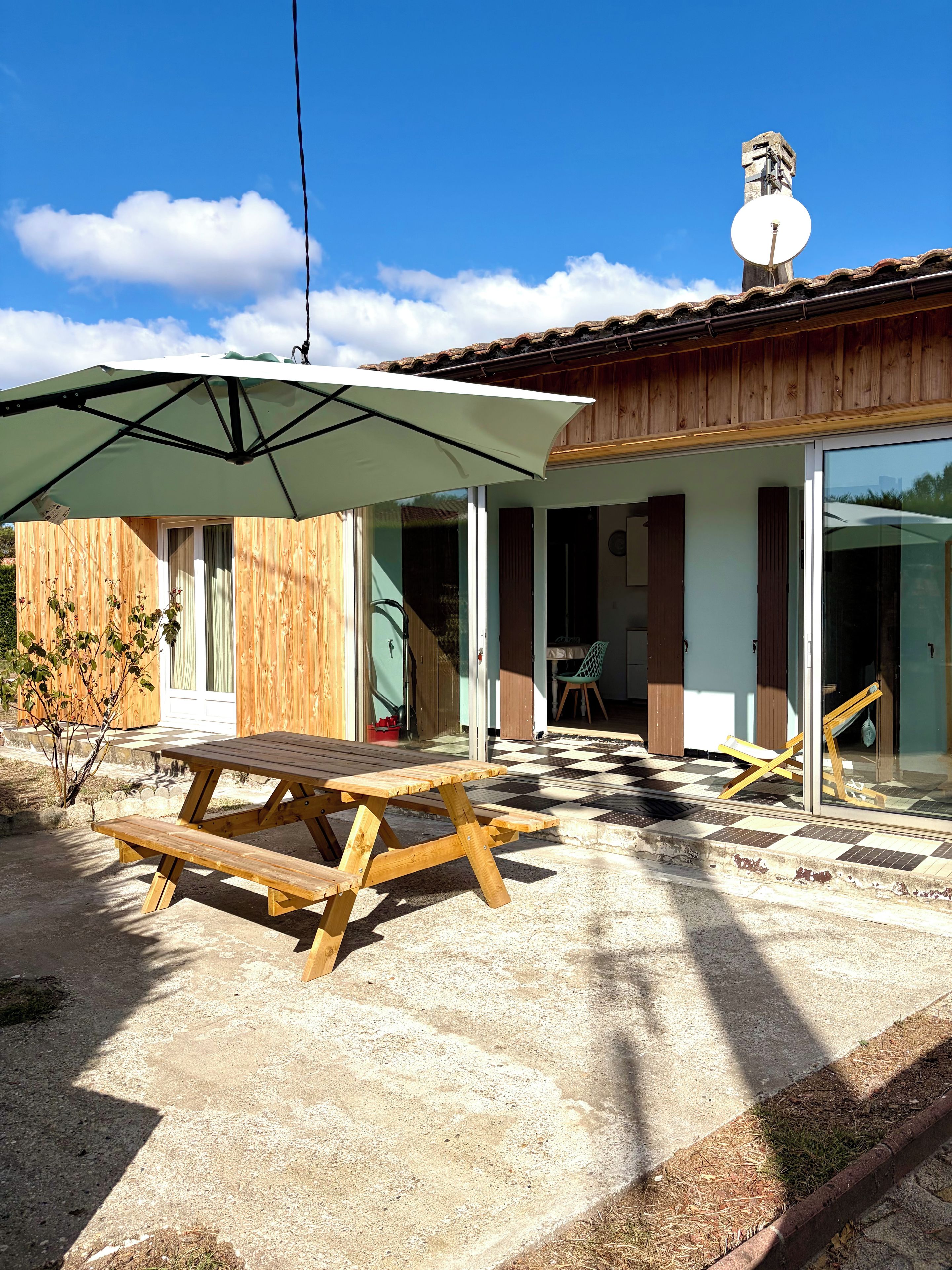 A wooden patio with a picnic table and umbrella, a checkered floor, and a building with a satellite dish.