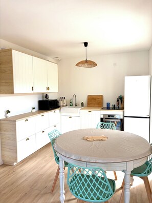 A modern kitchen with white cabinets, a round table, and teal chairs. - An Autumn Getaway in Cap Ferret, Amid Pine Trees and the Lagoon (Lège-Cap-Ferret)