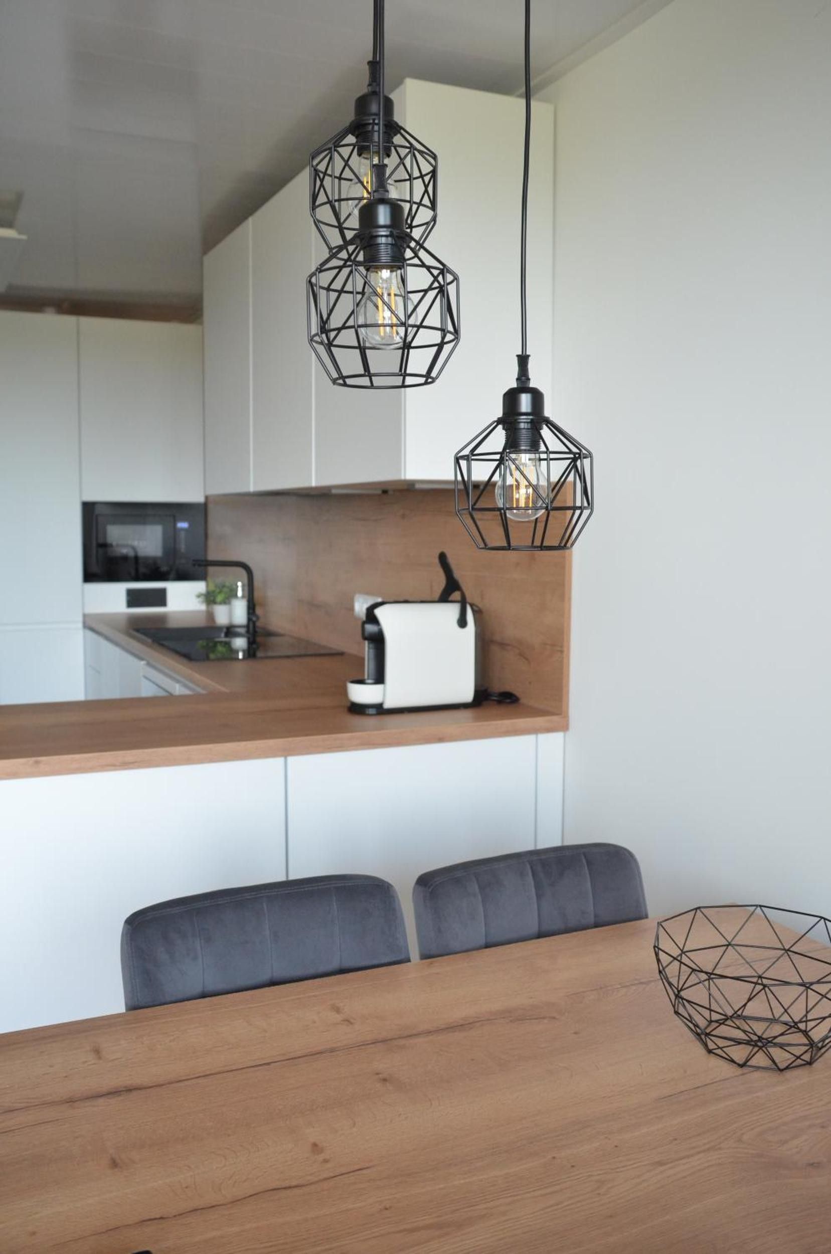 A modern kitchen with a wooden countertop, a white toaster, and two black geometric pendant lights.