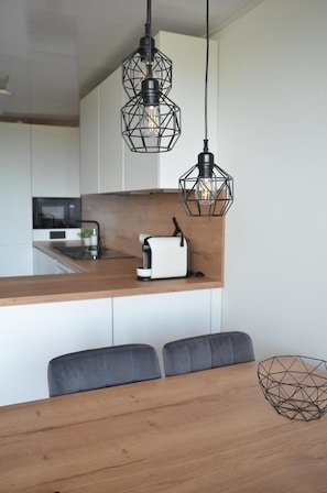 Eine moderne Küche mit einer Holz Arbeitsplatte, einem weißen Toaster und zwei schwarzen geometrischen Pendelleuchten.