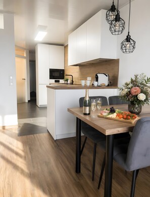 Una cocina moderna con armarios blancos, encimera de madera y un comedor con mesa dispuesta para dos.
