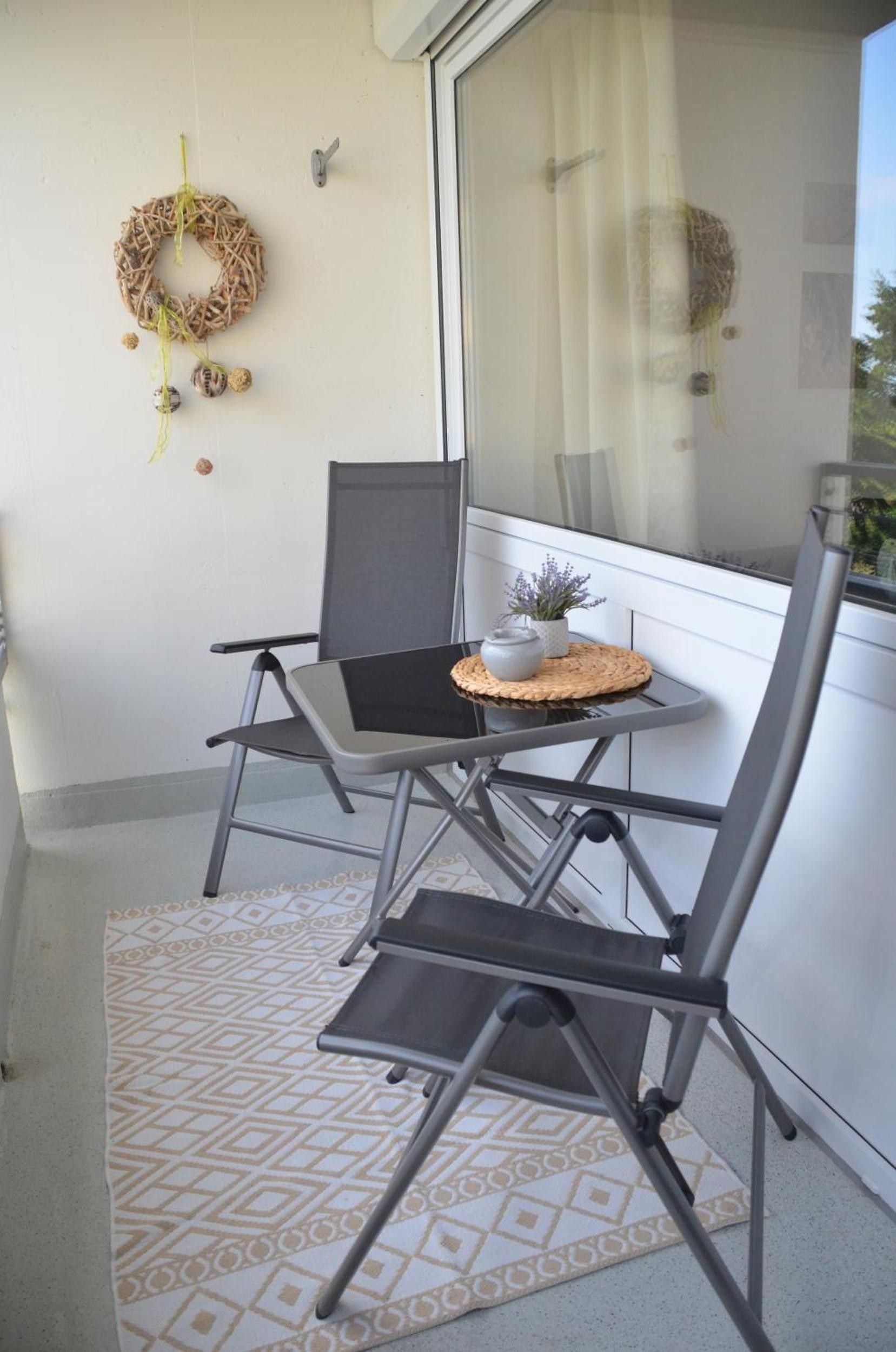 Un petit balcon avec deux chaises, une petite table ornée d’une plante et une guirlande décorative accrochée au mur.