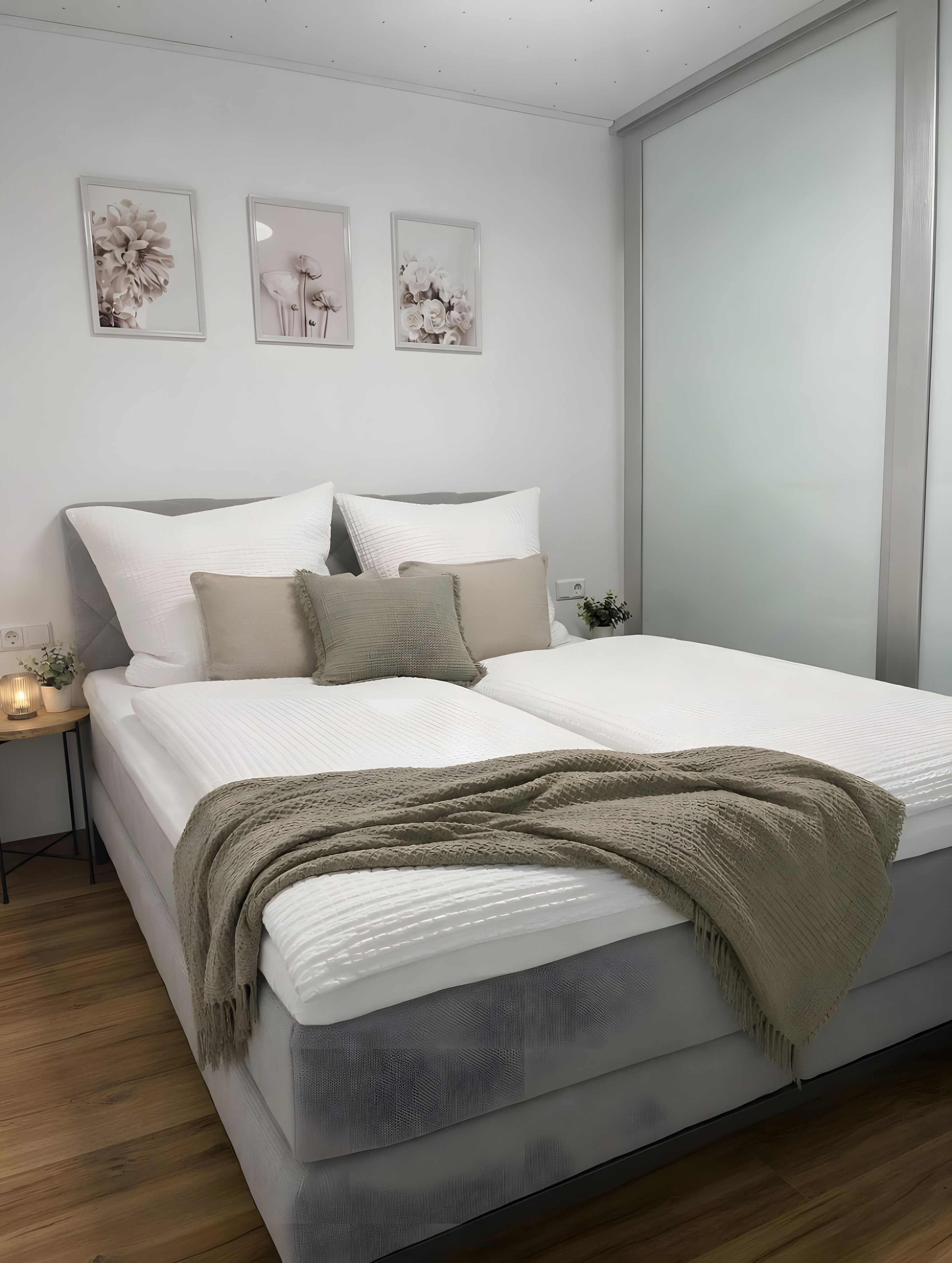 Un dormitorio moderno con una cama grande, una mesita de noche con lámpara y tres cuadros de flores en la pared.