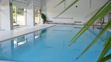 Ein beheiztes Hallenbecken mit klarem, blauem Wasser, umgeben von weißen Wänden und einem gefliesten Boden.