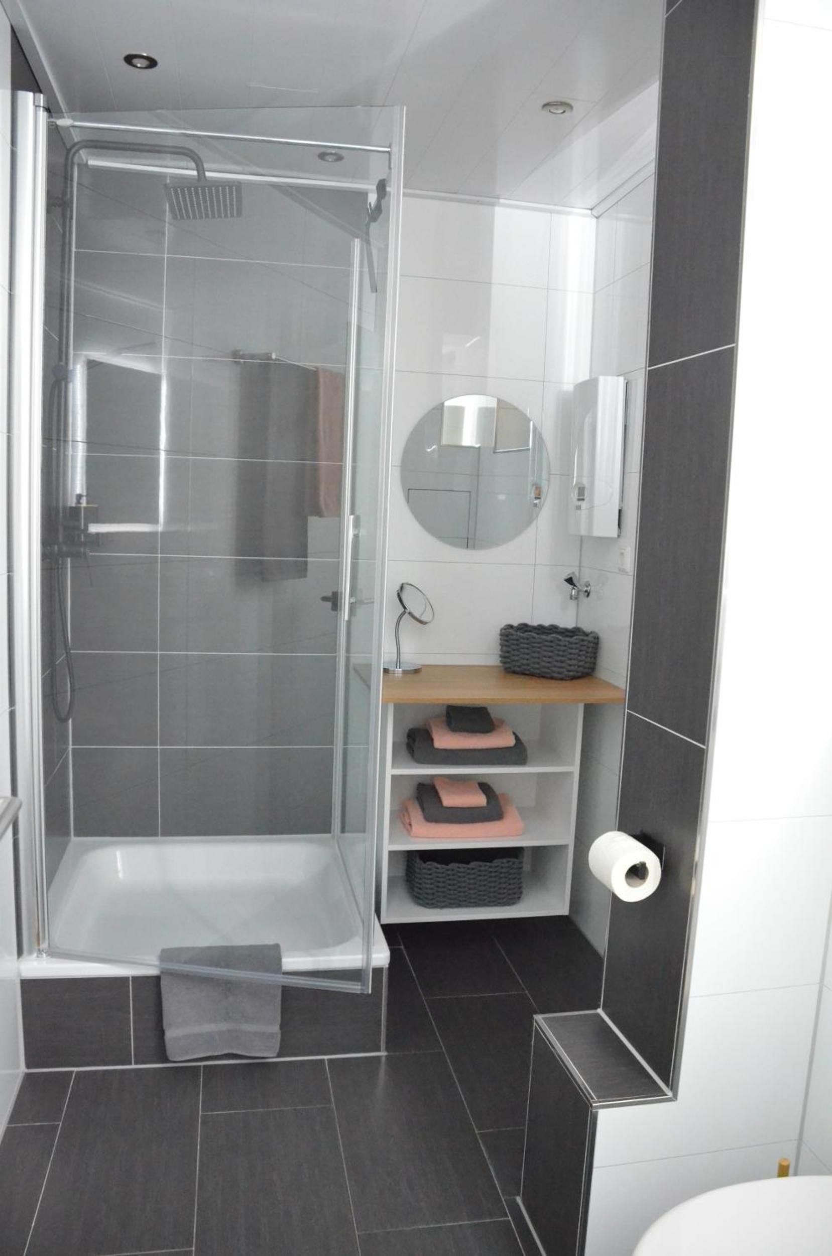 Ein modernes Badezimmer mit Duschkabine aus Glas, einem weißen Waschbecken mit Spiegel und einer Toilette.