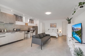 A modern apartment with a kitchenette, a grey sofa, a bed, and a large TV. - Casa Martina Terrace and Garden (Arco)