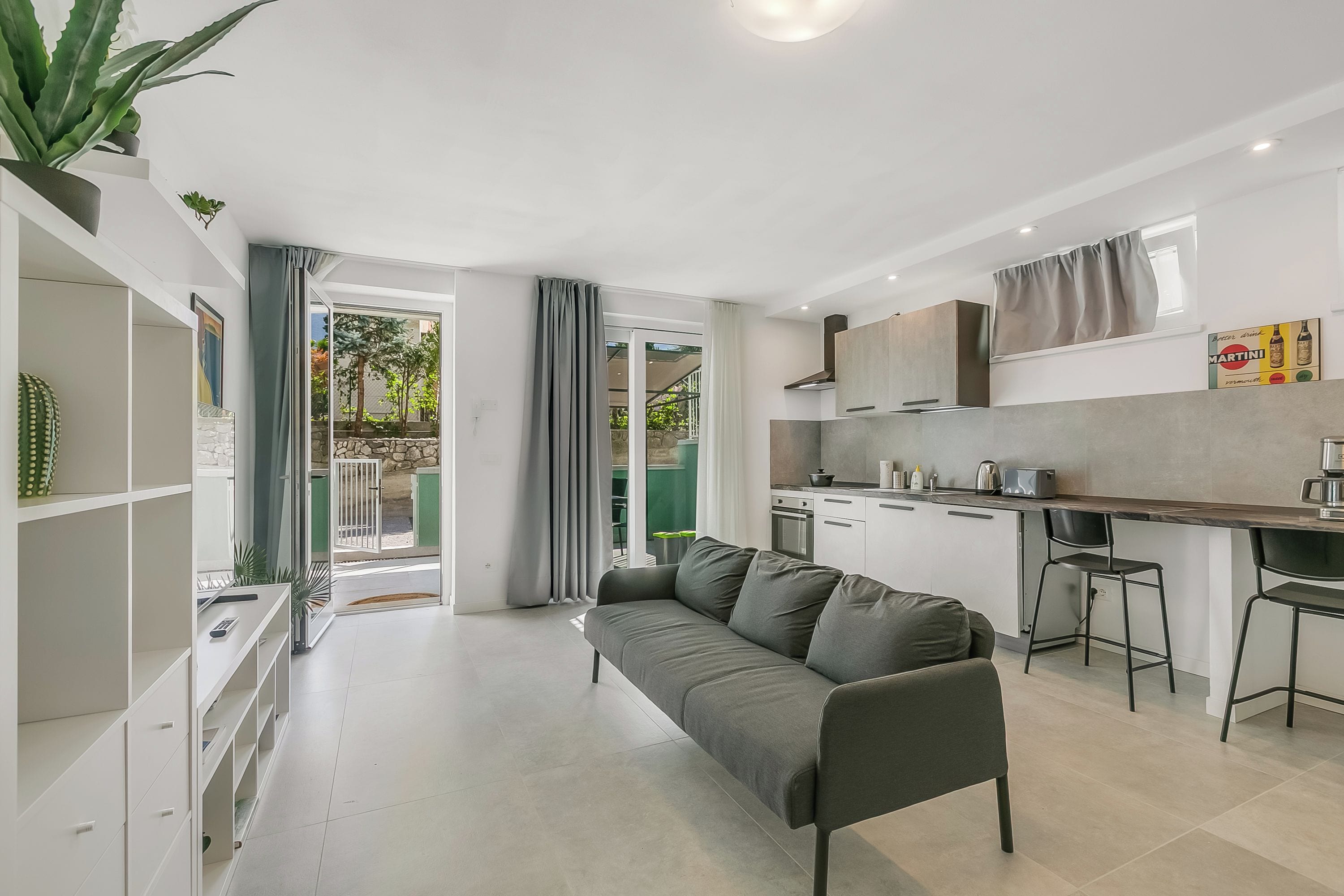 A modern apartment with a kitchenette, a grey sofa, and a dining area.