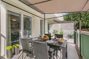 An outdoor dining area with a table set for two, surrounded by wicker chairs, under a retractable awning. - Casa Martina Terrace and Garden (Arco)