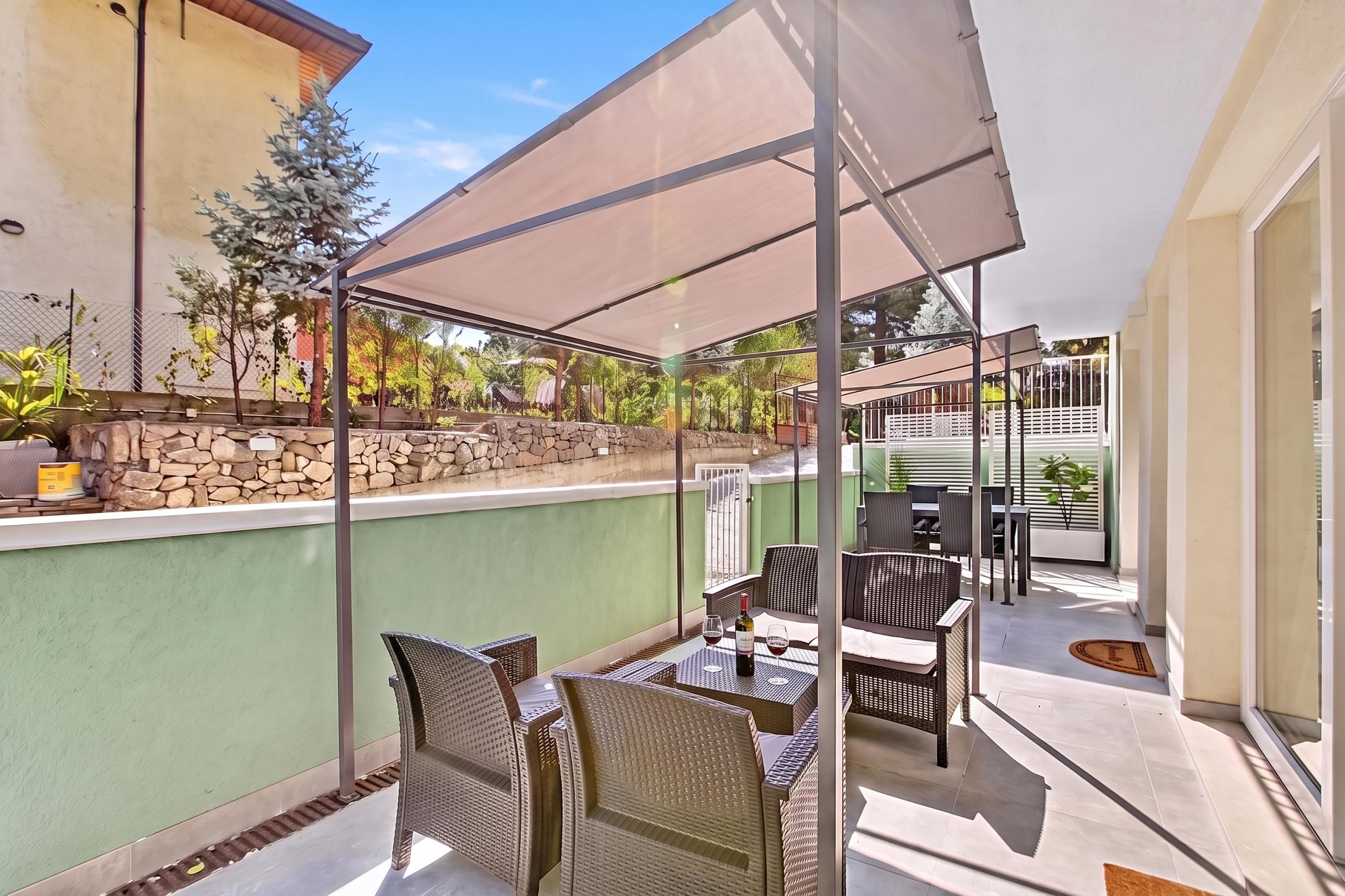 Un espace extérieur aménagé en terrasse, avec des meubles en osier, une table sur laquelle se trouvent une bouteille et des verres, et un mur en pierre.