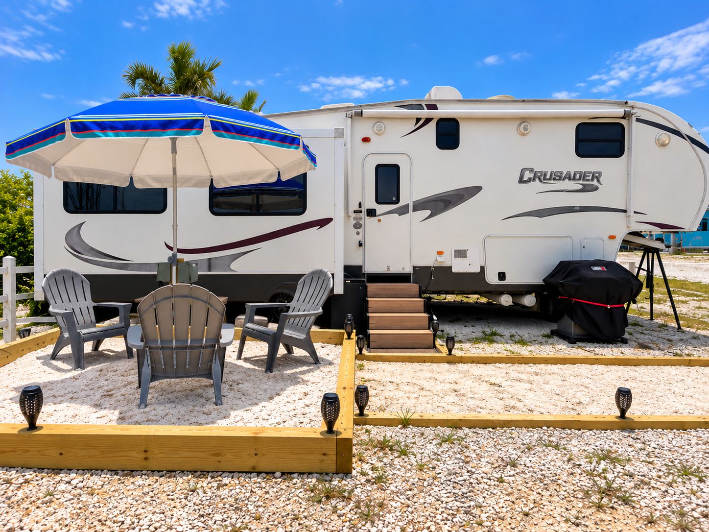 A recreational vehicle with a 'CRUSADER' logo, a covered outdoor seating area with chairs, and a grill.