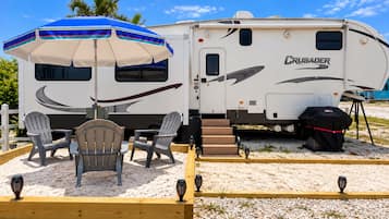 A recreational vehicle with a 'CRUSADER' logo, a covered outdoor seating area with chairs, and a grill.