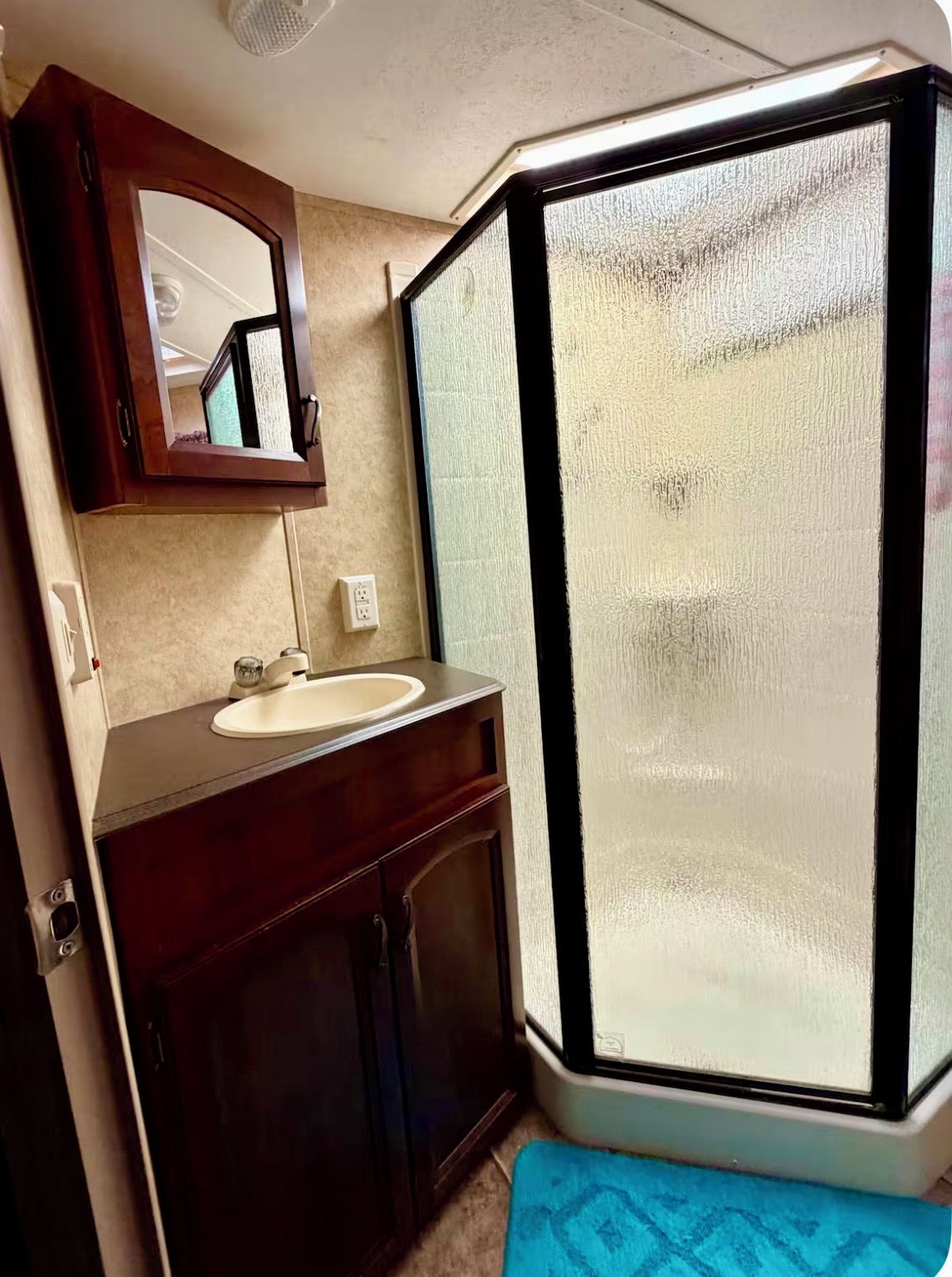 A bathroom with a sink, mirror, and shower enclosure.