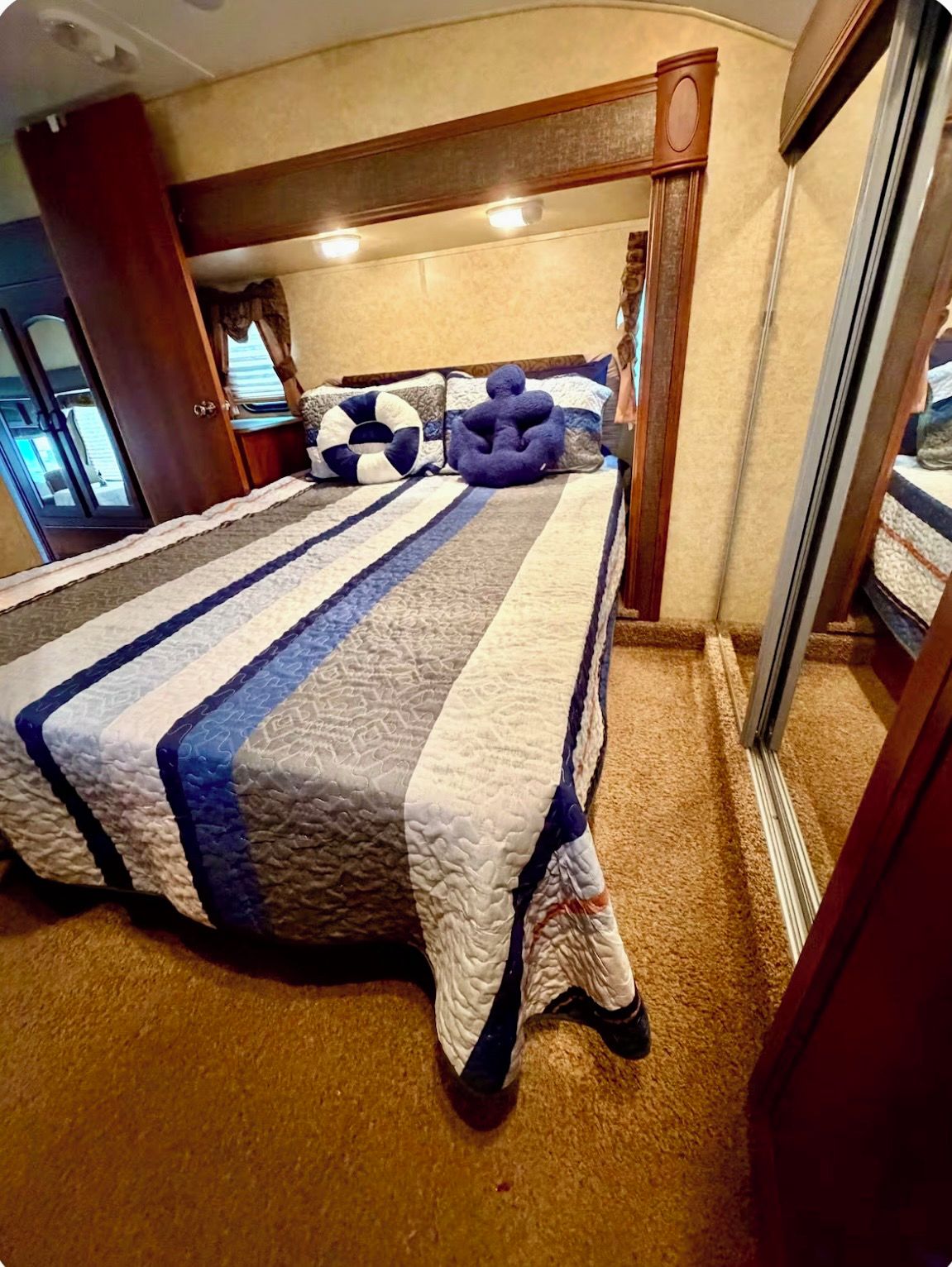 A bed with a striped quilt, a headboard, and a mirror on the wall.