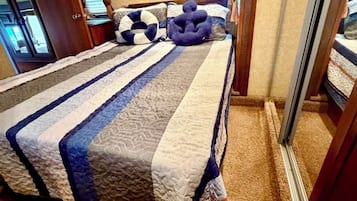 A bed with a striped quilt, a headboard, and a mirror on the wall.